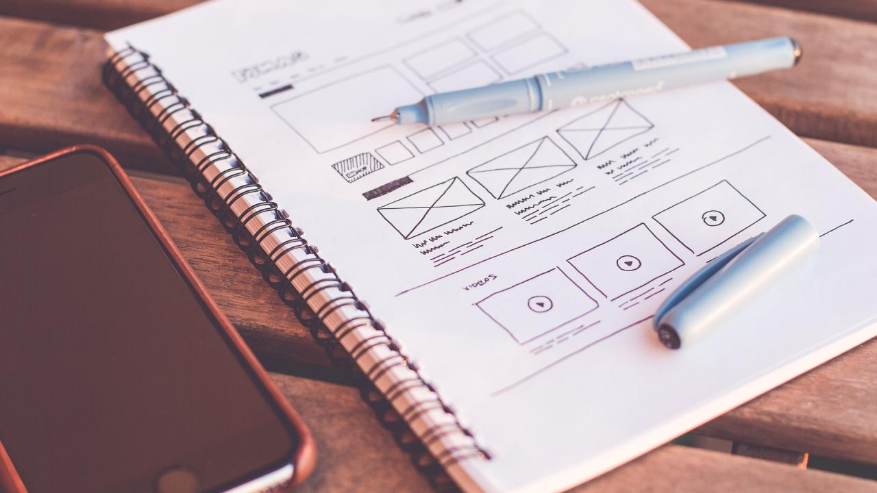 A photograph of a spiral notebook page filled with wireframe designs for a web page.