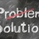 A chalkboard with the words problem and solution, with a red line scratched through the word problem.